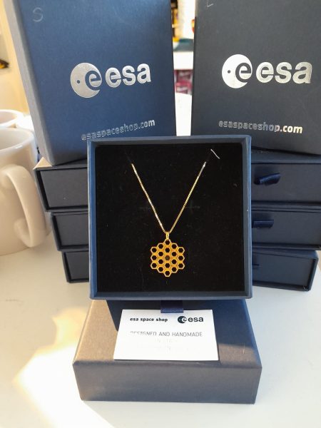 A gold coloured pendant in the shape of the JWST mirror. It looks similar in shape to honeycomb