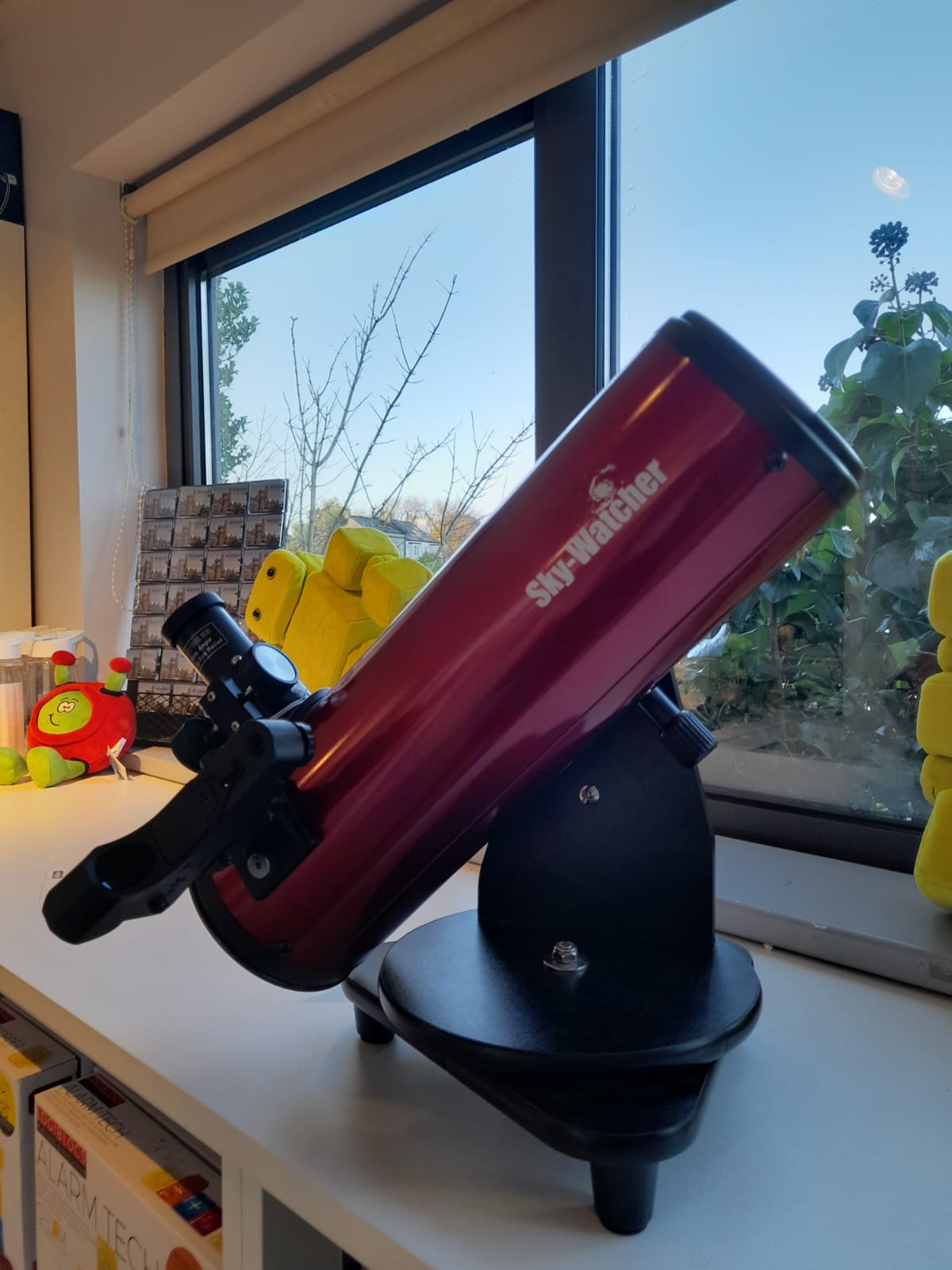 A desktop telescope placed on a windowsill looking outwards. It is red on a black mount