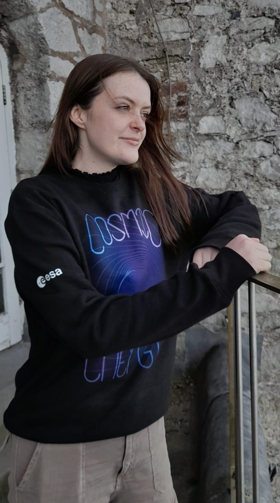 A photo of a woman wearing a black ESA, Cosmic Energy sweater.